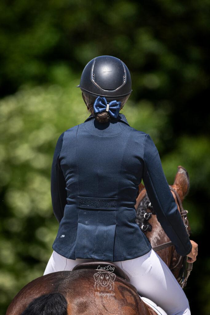 Cavalière vue de dos avec sa bombe d'équitation lors d'un concours ou entraînement.