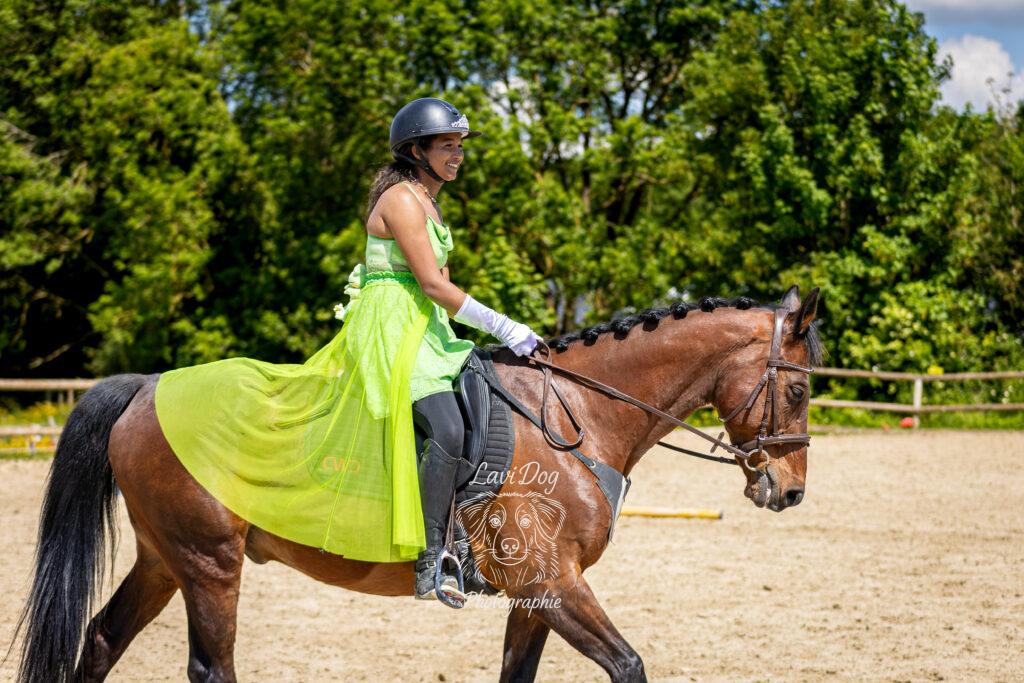 Cavalière vêtue d'un haut jaune sur un poney ou cheval alezan.